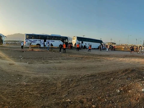 צוות ונוסעים ליד שיירת אוטובוסים במדבר, בשעת השקיעה